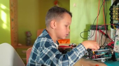 Çocuk masada oturur oyuncak arabaların tekerleklerini uzaktan kumandayla hareket ettirir..