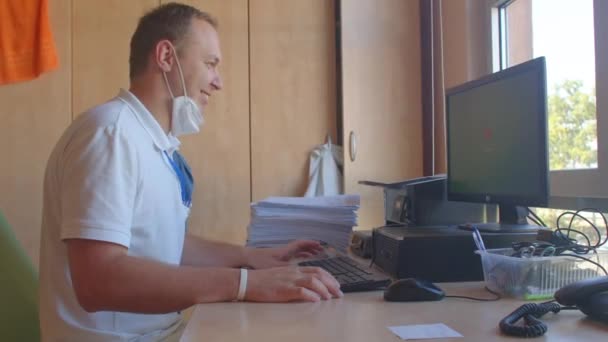 Un operaio con una maschera sulla barba usa un computer a un tavolo in un ufficio — Video Stock