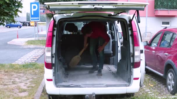En manlig lastare städar bilen efter jobbet. Han sopar golvet. — Stockvideo