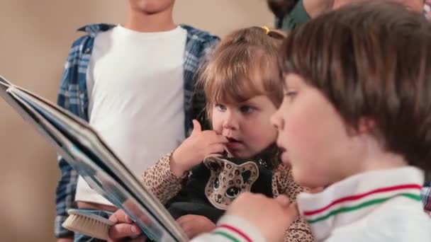 Un padre con muchos hijos lee un libro con niños. Centrar la atención historia. — Vídeos de Stock