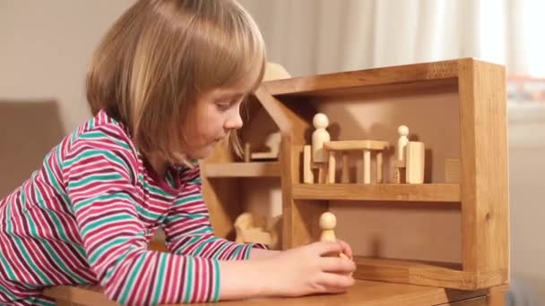 Skup się na grze child girl puts figures in wooden house with hands — Wideo stockowe