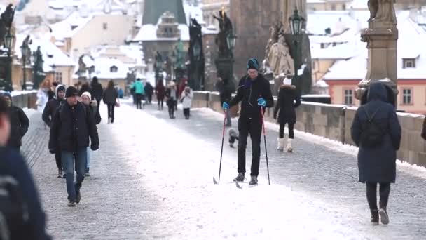 Homem esquiando faixa de neve em Charles Bridge. Ele apoia-se em paus, faz um esforço. — Vídeo de Stock