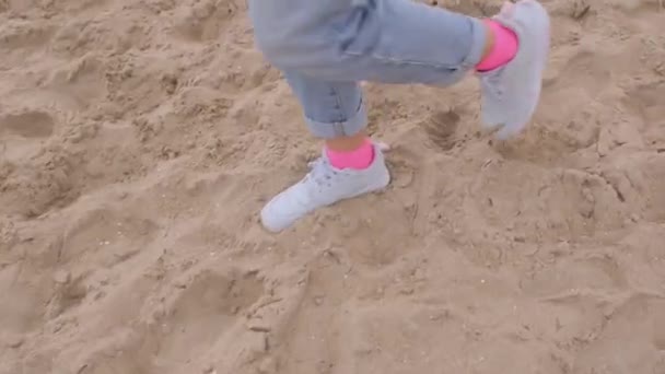 ピンクの靴下と白いスニーカーの女性の足は砂のビーチでステップ. — ストック動画