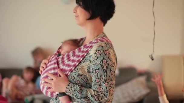 Padres de familia numerosa. Madre con el recién nacido en un portabebés en casa. — Vídeos de Stock