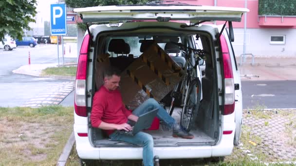Muž v červeném oblečení používá notebook v kufru auta. Zpracování digitálních dat. — Stock video