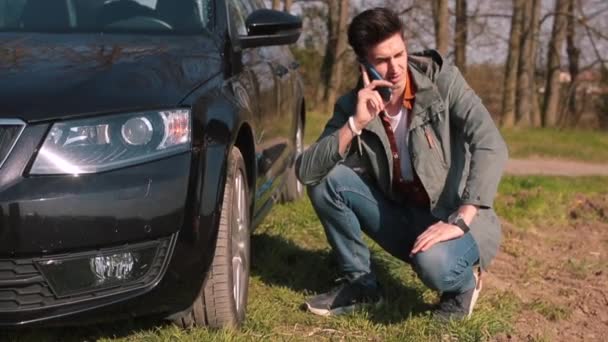 Een man is aan de telefoon met een auto reparatie, hij zit vast op een kapotte auto.. — Stockvideo