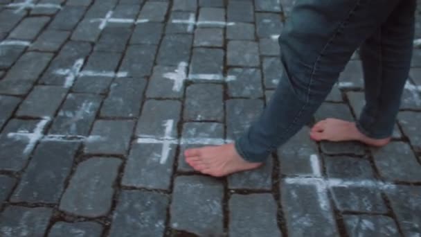 Los pies desnudos del hombre dan pasos a lo largo de la acera de piedra. Las cruces están pintadas en la acera — Vídeo de stock