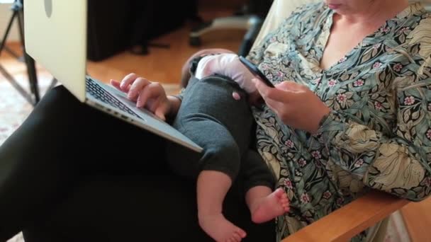 Die geschäftige Mutter eines Neugeborenen telefoniert mit dem Computer auf dem Schoß. Kein Gesicht. — Stockvideo