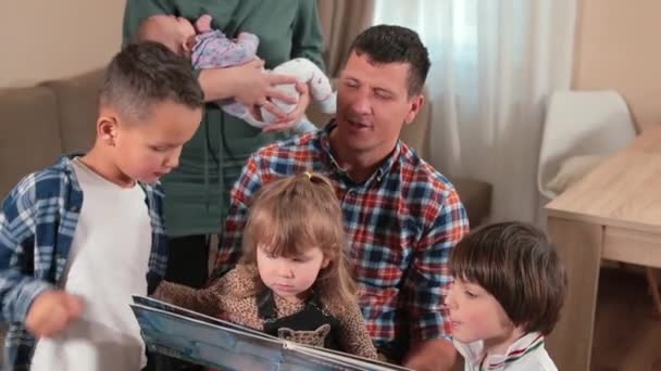 Großfamilie liest Buch zu Hause Vater hält Tochter im Arm, neben seinen Söhnen. — Stockvideo
