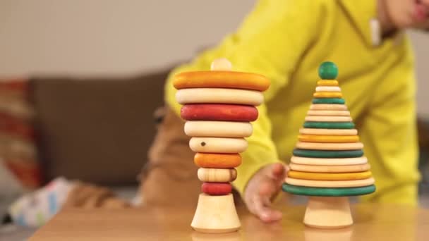 Подросток в желтой одежде играет с деревянными игрушками на столе. — стоковое видео