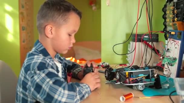 Boy sits at table, assembles toy car. He says message is cutting off item — Stock Video