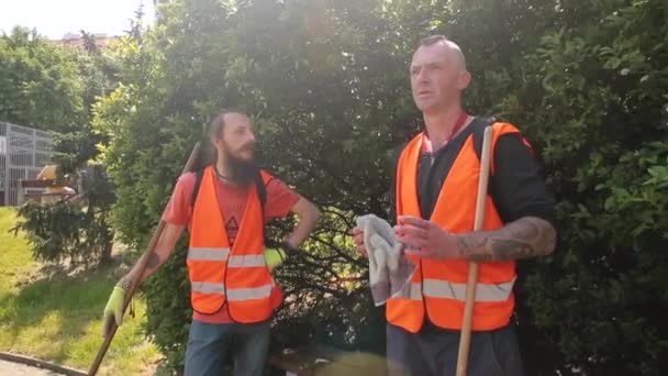 Dos trabajadores chalecos naranjas hablan durante el descanso. Esperan la acción del plan de trabajo. — Vídeos de Stock