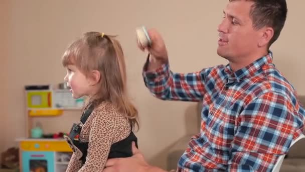 Papá peinando el pelo de su hija. Él hace visiones con peine chica se mueve, alegría. — Vídeos de Stock