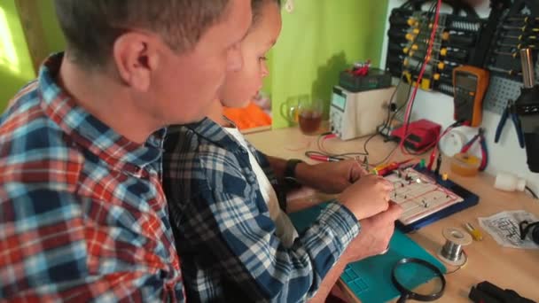 El muchacho hace la junta caliente usando el soldador mira lupa, control de calidad — Vídeos de Stock