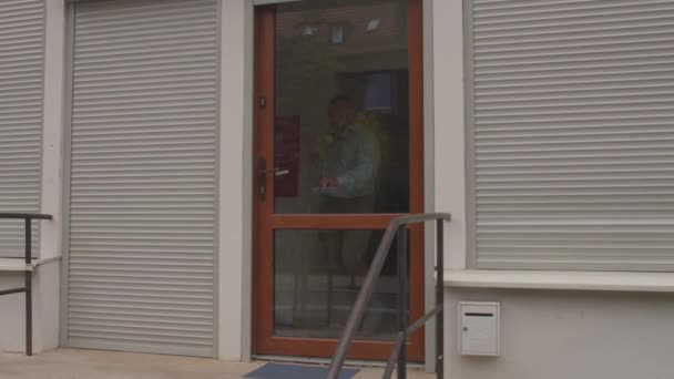 Man walks out door of the building. He uses hand on door handle. End work. — Stock Video