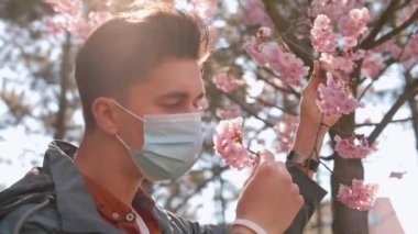 Maskeli adam çiçekleri kokluyor. Güneşli bir gün. Yasak halka açık bir yerde maskeyi çıkarıyor.