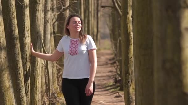 Mulher inspiradora se move ao longo da estrada da floresta. Ela toca as mãos das árvores, canta música — Vídeo de Stock