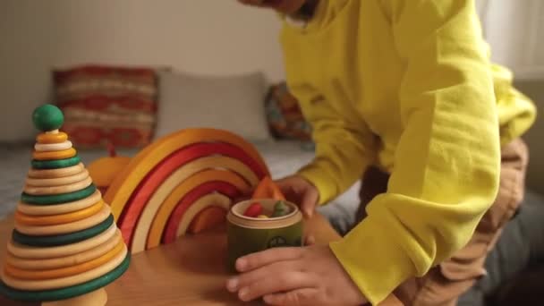 어린이는 탁자 위에 놓인 나무 장난감에 관심이 있다. 그는 나무로 만든 형상을 펼쳐 놓는다. — 비디오