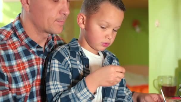 Apa és fia az asztalnál vizsgálják a részleteket. Együtt javítják a játékokat. — Stock videók