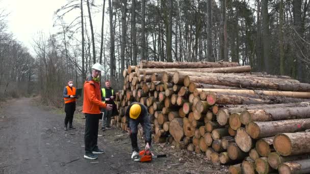 Hij houdt een gereedschap in zijn handen, start de motor. Veiligheid op het werk. Stapels bomen — Stockvideo