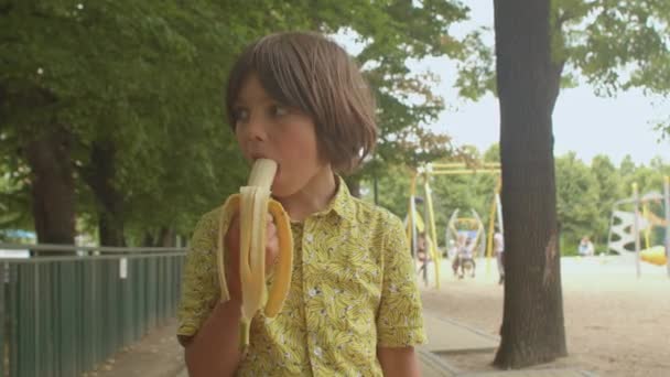 Niño en una camisa amarilla está comiendo un plátano estimular la producción de endorfinas. — Vídeos de Stock