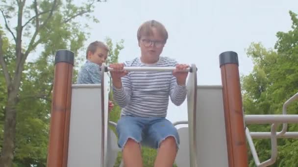 A Down-szindrómás fiú csúszdázik. A gyermekkori öröm ragyogó pillanata. — Stock videók