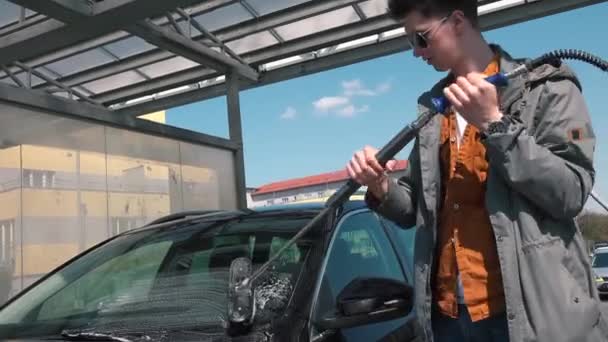 Limpieza de la suciedad después de un viaje. Hombre con gafas lava el coche con las manos. — Vídeo de stock