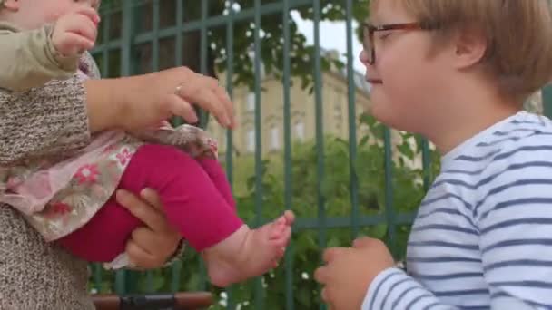 O menino da síndrome de Down toca examina os pés da criança bebê. Aquisição de novos — Vídeo de Stock