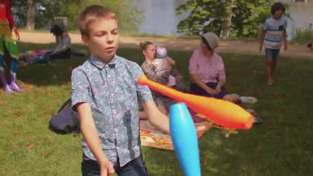 Garçon essaie de jongler avec les clubs de jonglerie de couleur, style de vie à l'extérieur. Jouets pour enfants. — Video
