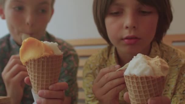 Два брати їдять морозиво з ложкою в кафе тримають його вафельним конусом стукаючи — стокове відео