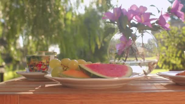 Masada taze kahvaltı. Meyve, cam, vazoda çiçekler. Güneş ışığı. — Stok video