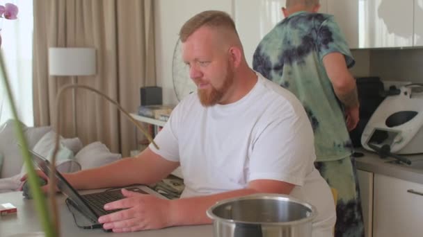 L'homme barbu utilise une table d'ordinateur. Le partenaire ramasse la tasse avec un cocktail. — Video