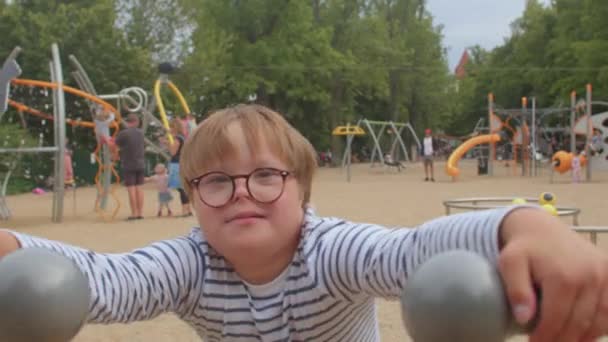 Potret anak laki-laki dengan sindrom Down bermain di taman bermain. peralatan bermain inklusif — Stok Video