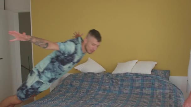 Veselý chlap skočí na postel, parťák ho přikryje dekou, ofinou s polštářem. — Stock video