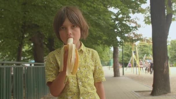 Adolescente de cabelo longo na camisa desenho banana come banana crescente força corpo — Vídeo de Stock