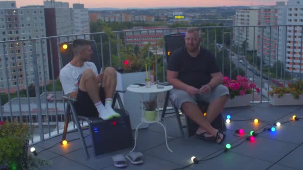 Ga 's avonds uit met twee mannen op het terras. Ze zitten op stoelen met kleurenverlichting. — Stockvideo