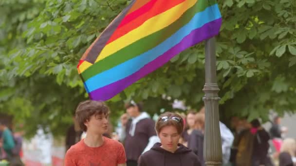 Två killar rör sig nära hbt-flaggan i en stadspark offentligt uttryck för frihet. — Stockvideo