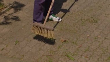 Şehir parkında iki işçi caddeyi tarıyor. Temizlik yapıyorlar. Toplama toprağı.