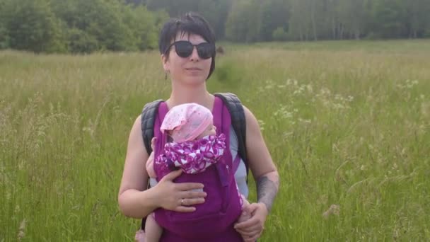 Jeune mère se déplace herbe près de forêt enfant attaché corps, elle utilise fronde. — Video