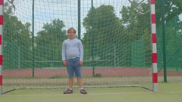 Down syndrom pojke med glasögon står vid målet för en fotboll. — Stockvideo