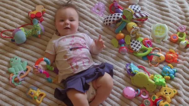 小さな女の子はおもちゃを着てベッドの上に横たわっている。近くに独立した遊び道具がある — ストック動画