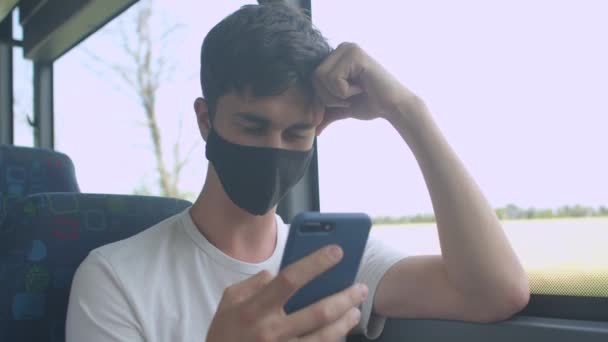 Homme masque noir utilise le téléphone près du mouvement de la fenêtre du bus. Regardez l'écran le long de la route — Video