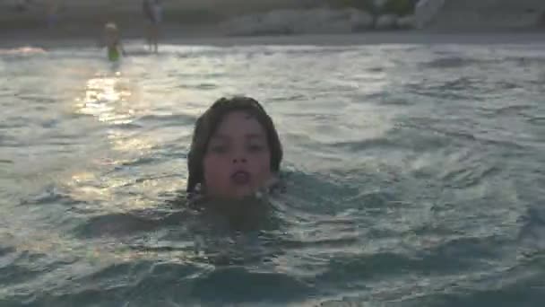 Portrét dítěte plovoucího v moři u pobřeží večer při západu slunce. — Stock video