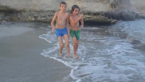 Ευτυχισμένα αγόρια τρέχουν κατά μήκος των κυμάτων της παραλίας. — Αρχείο Βίντεο