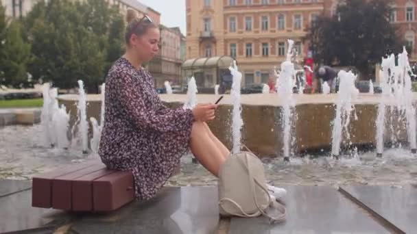 Telefonní použití ve městě dívka úzkostlivě čte zprávy pomocí fonní město fontány — Stock video