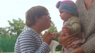  Genç kız annesinin kollarındaki kızla iletişim kuruyor..