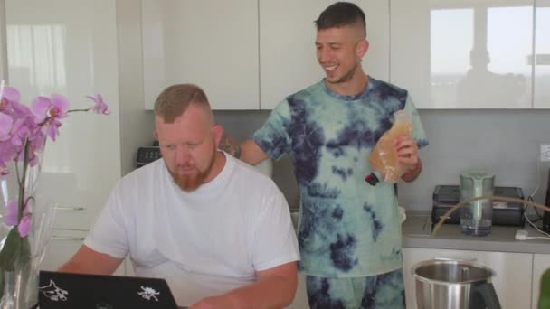 Dos chicos comienzan el desayuno cocina toma jugo nevera añade licuadora beso socio — Vídeo de stock