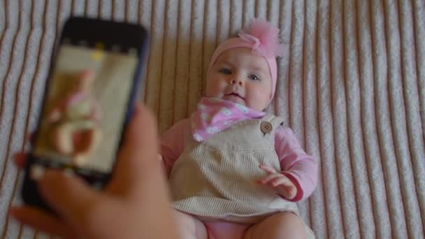 Дитяча дівчинка малюк позує лежачи ліжко фото рука тримає телефон робить фотографії — стокове відео