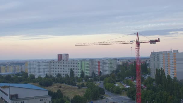 Una gru contro un paesaggio urbano serale. Sviluppo di una zona residenziale. — Video Stock