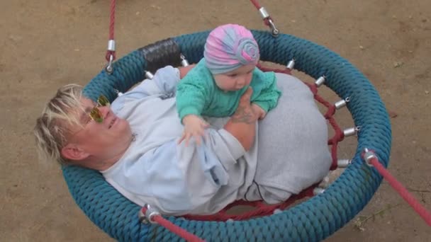 Disabled woman is riding on swing with child. She holds him in her arms, talks — Stock Video
